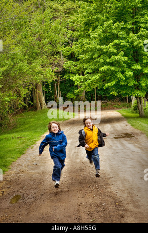 Due ragazzi fratelli gemelli che corre verso la telecamera racing giù un percorso sterrato uscendo dal bosco Foto Stock