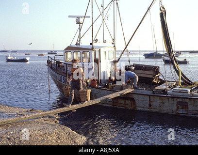L'archivio degli anni '1980 visualizza gli uomini al lavoro su una tavola che usano i giogo per trasportare cesti di molluschi dal peschereccio Leigh degli anni '80 sul mare Southend Essex Inghilterra Regno Unito Foto Stock