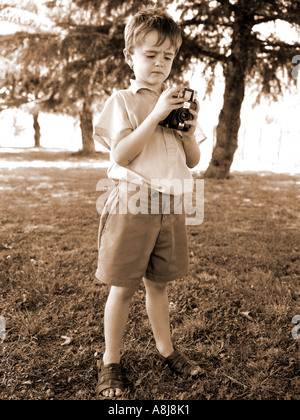 Seppia Immagine di bambino in maglia grigia e pantaloncini di flanella tenendo un bakerlite fotocamera e scattare una foto Foto Stock