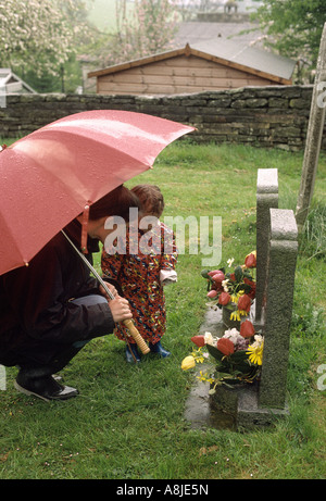 La madre e il bambino guardando la tomba pietre in un cimitero Foto Stock