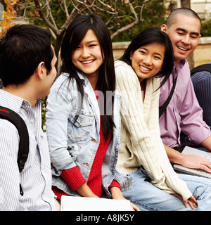 Quattro studenti del college seduto in un campus universitario e sorridente Foto Stock