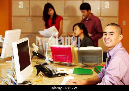 Ritratto di un uomo di affari utilizzando un computer con tre dirigenti aziendali che funziona in background Foto Stock