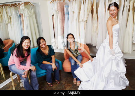 Tre giovani donne ad aiutare il loro amico provare su un abito da sposa in un negozio nuziale Foto Stock