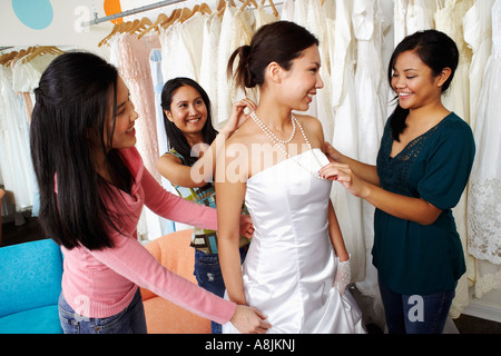 Tre giovani donne ad aiutare il loro amico provare su un abito da sposa in un negozio nuziale Foto Stock