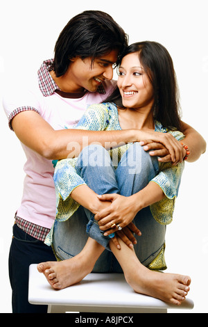 Giovane uomo abbracciando una giovane donna da dietro di lei e sorridente Foto Stock