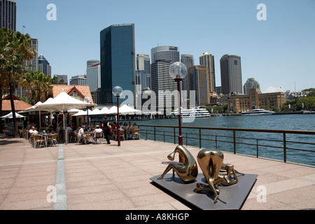 Persone mangiare e bere fuori al Harbour cafe su Opera Quay con sculture e edifici per uffici a Sydney nel Nuovo Galles del Sud. Foto Stock