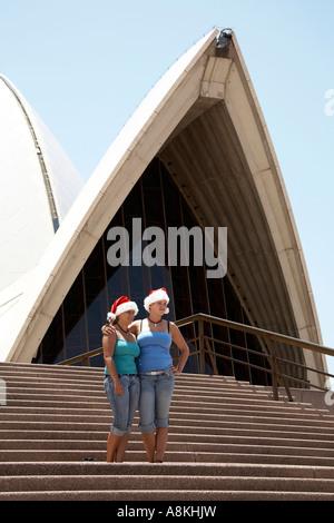 Due donne o ragazze che posano con Babbo Natale cappelli sui gradini davanti della Opera House di Sydney, Nuovo Galles del Sud Australia NSW Foto Stock