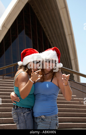 Due donne o ragazze che posano con Babbo Natale cappelli sui gradini davanti della Opera House di Sydney, Nuovo Galles del Sud Australia NSW Foto Stock