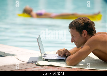 Un uomo a bordo piscina con un computer portatile Foto Stock