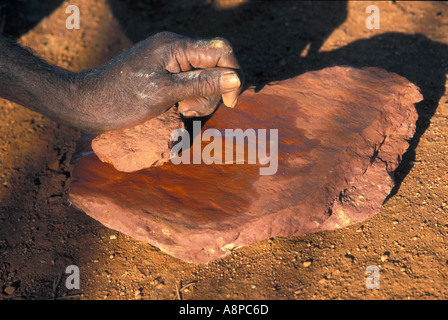 Uomo Aborigeno di sfregamento ocra rossa sulla roccia per produrre polvere rossa per la pittura su organismi per la tradizionale cerimonia rituale Australia Foto Stock