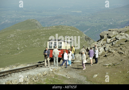 Treno di montagna Snowdon e passeggeri in visita turistica che aspettano di rientrare a bordo a metà strada con Snowdonia Gwynedd North Wales UK paesaggio oltre Foto Stock