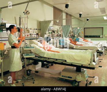 Giovane femmina infermiera in ospedale con pazienti in reparto cure intensive. Foto Stock
