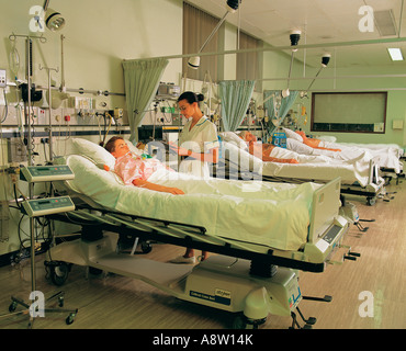 Giovane femmina infermiera in ospedale con pazienti in reparto cure intensive. Foto Stock