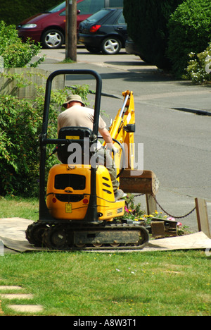 Uomo guida mini pista posa escavatore cingolato attraverso giardino prato domestico fronte su legno compensato fogli di protezione Essex Inghilterra UK Foto Stock