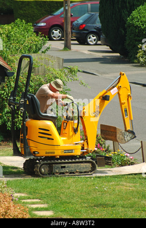 Uomo che controlla Mini escavatore che striscia attraverso il prato giardino anteriore domestico su fogli di compensato stabiliti per la protezione Essex Inghilterra UK Foto Stock
