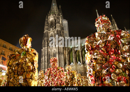 Di notte, figure dell’installazione ‘Trash People’ di HA Schult si trovano davanti alla cattedrale di Colonia illuminata. La figura in primo piano a destra è interamente rivestita di lattine di Coca-Cola rosse accartocciate, mentre le figure a sinistra sono realizzate con scarti di lamiera nei toni del marrone ruggine e dell’oro. Colonia, Renania Settentrionale-Vestfalia, Germania Foto Stock