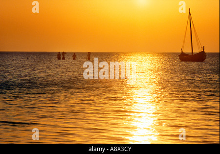 Ancorata Viking s di lunghezza della nave contro il tramonto e la gente di balneazione in mare poco profondo Foteviken, Skane, Svezia Foto Stock
