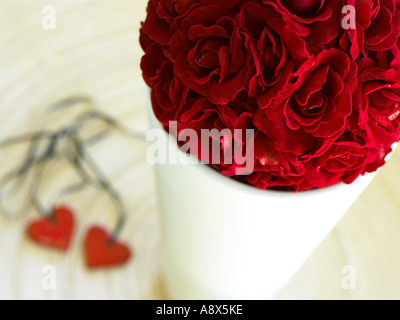 Sfera di rose rosse in un pallido vaso colorato sul tavolo con due cuore rosso collane accanto Foto Stock