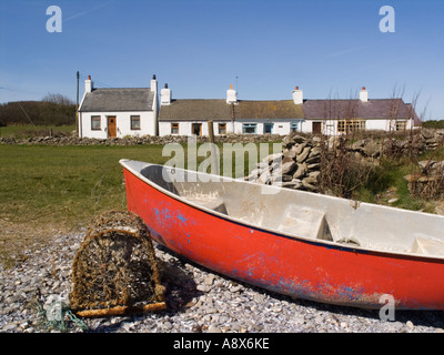 Barca Rossa e lobster pot sulla spiaggia di ciottoli con riga bianca di case di pescatori in Moelfre Anglesey North Wales UK Gran Bretagna Foto Stock