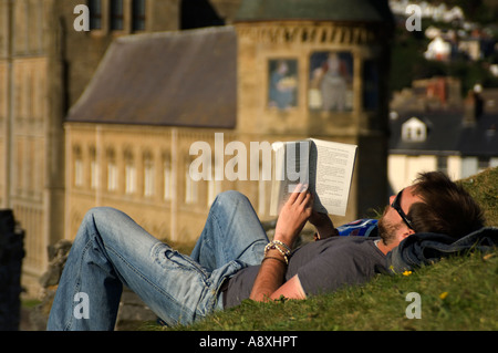 Uomo disteso sulla sua schiena sull'erba la lettura di un libro con la University of Wales Aberystwyth Old College in background; estate Foto Stock