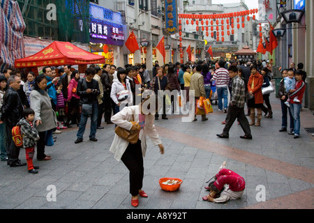 Ragazza cinese Street Performer e mendicante Shang Xia Jiu Square una trafficata strada pedonale per lo shopping mall a Guangzhou in Cina Foto Stock