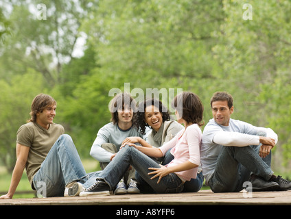 Un gruppo di giovani amici adulti seduti intorno all'esterno insieme Foto Stock