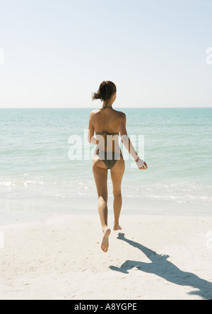 Giovane donna sulla spiaggia a correre verso l'oceano, vista posteriore Foto Stock
