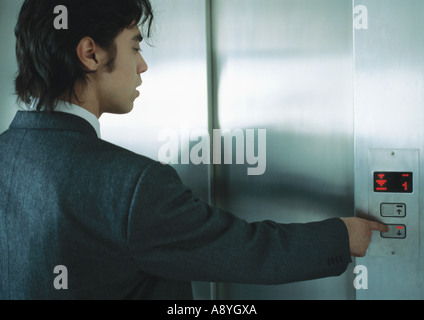 Giovane uomo in tuta spingendo il pulsante per ascensore Foto Stock