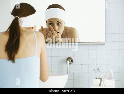 La donna in piedi di fronte a specchio bagno, inserimento di lente a contatto Foto Stock