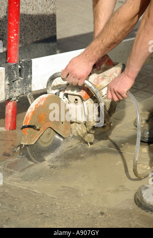 La pavimentazione di stabulazione di riparazione lavori in corso due operai con disco di taglio & water spray per inumidire giù il controllo delle polveri Londra Inghilterra REGNO UNITO Foto Stock