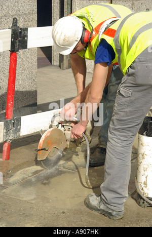 La pavimentazione di stabulazione di riparazione lavori in corso due operai con disco di taglio & water spray per inumidire il controllo verso il basso e la polvere Foto Stock