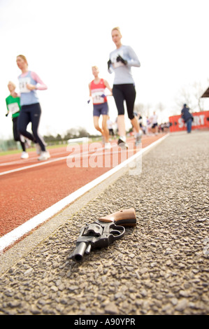 A partire pistola lasciata a terra vicino alla via di corsa con fuori fuoco gli atleti in esecuzione in background Foto Stock