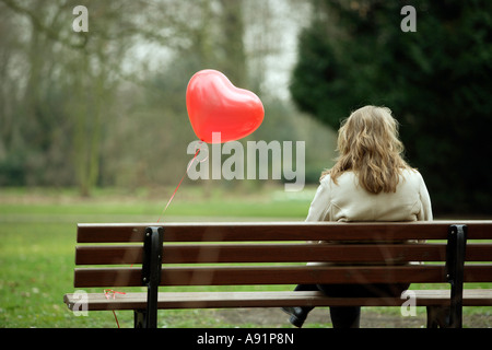 Una giovane donna si siede da solo su una panchina nel parco Foto Stock