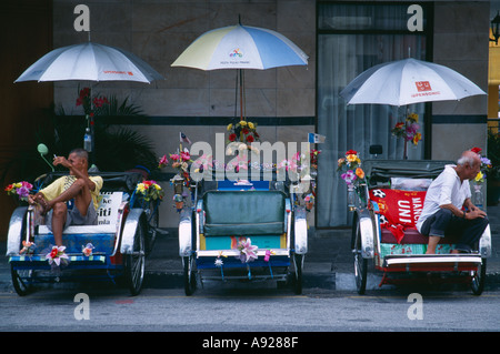 MALAYSIA Penang Georgetown tre risciò bicicletta decorata con fiori e bandiere con due piloti in appoggio dal lato della strada Foto Stock