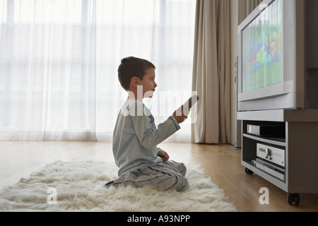 Ragazzo (7-9) seduto sul pavimento, guardando cartoni animati in televisione Foto Stock