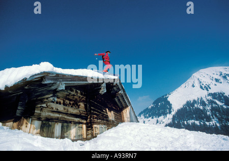 Sciatore su monoboard saltare giù dal tetto del chalet Leysin Svizzera Europa Foto Stock