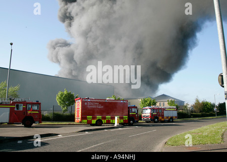 Il servizio antincendio veicolo di controllo sotto il pennacchio di fumo e i detriti che cadono a fuoco al magazzino medico coleraine Foto Stock