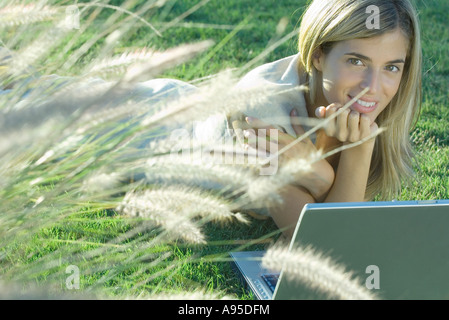 Giovane donna che giace nel campo con il computer portatile Foto Stock