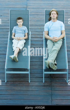 Giovane uomo e ragazzo seduto sulle sedie a sdraio ascoltando gli auricolari, gli occhi chiusi Foto Stock