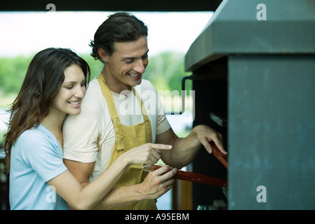 Giovane avente cookout insieme, donna che puntano a barbecue Foto Stock