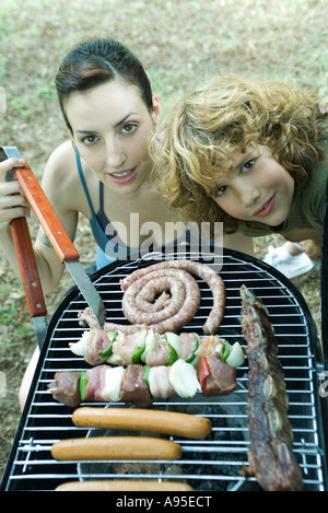 Famiglia avente cookout, donna e bambino vicino al barbecue, sorridente in telecamera Foto Stock