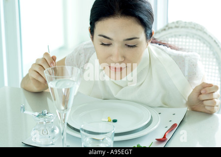 Donna seduta al set table, indossando il tovagliolo attorno al collo, vitamine sulla piastra Foto Stock