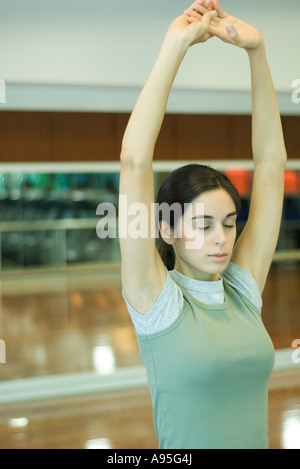 Giovane donna stretching overhead di armi a occhi chiusi Foto Stock