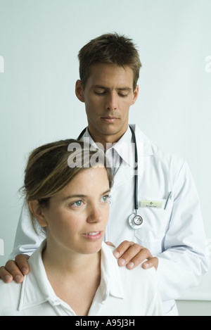 Dottore in piedi dietro la donna e le mani sulle sue spalle Foto Stock