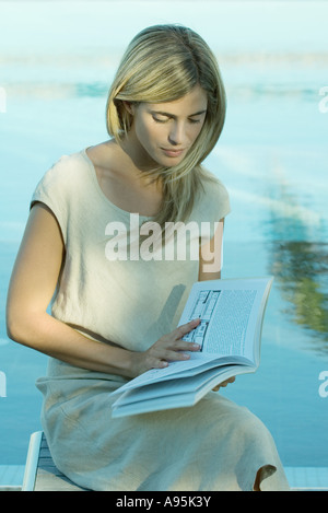 Donna seduta e la lettura prenota, acqua in background Foto Stock