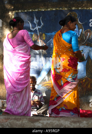 Le donne indiane che comprano gli articoli di pooja dallo stallino davanti al murale di Shiva al carro armato di Banganga, Mumbai, India Foto Stock