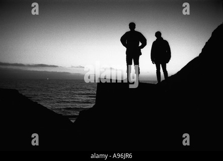 Due uomini stavano in piedi sulla seconda guerra mondiale porta pillole fortificazioni al tramonto guardando oltre il mare a unidentifeid luce all'orizzonte Foto Stock