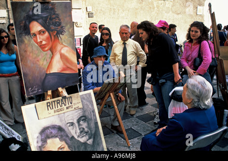 Sicilia Taormina - artista di strada pittura / disegno un sitter in piazza della città vecchia, curiosi Foto Stock