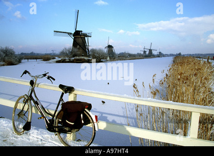 Mulini a vento del sito Patrimonio Mondiale dell'Unesco Kinderdijk in inverno con in primo piano la bicicletta sul ponte Foto Stock