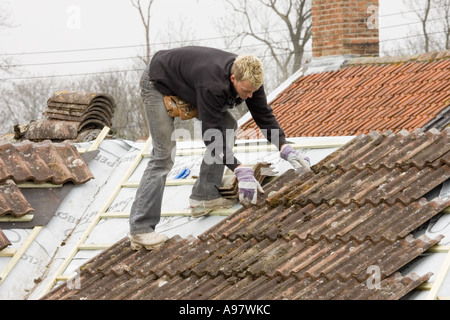 Un costruttore di montaggio di piastrelle su un tetto di una casa in estensione Foto Stock